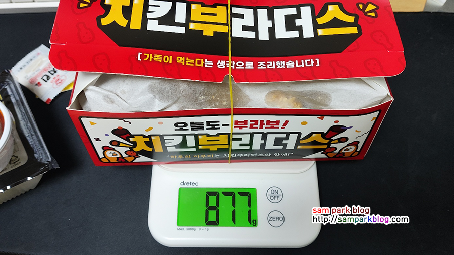 주방 저울 위에 치킨 박스를 올려놓고 무게 877g이 표시된 액정 화면 사진