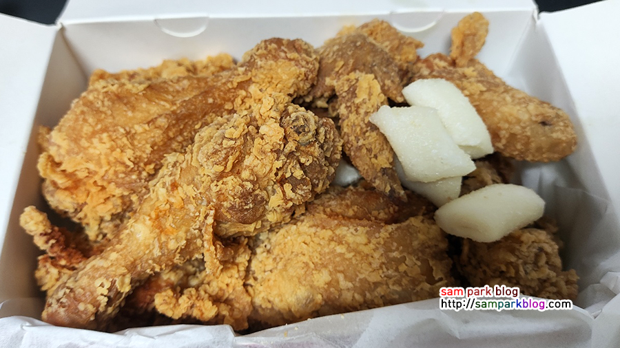 치킨 박스를 개봉하여 바삭한 후라이드 치킨과 위에 놓인 튀긴 떡 6개가 보이는 사진